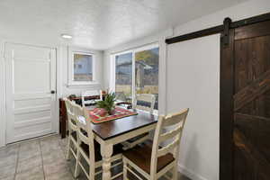 Dining space featuring a barn door, a textured ceiling, and light tile patterned floors