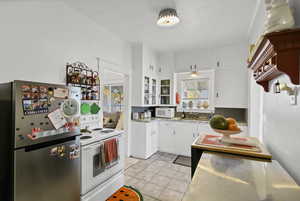 Kitchen with white cabinetry, white appliances, light tile patterned flooring, light countertops, and glass insert cabinets