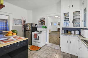 Kitchen with white cabinetry, white appliances, glass insert cabinets, light countertops, and ornamental molding