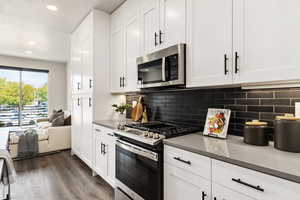 Kitchen featuring appliances with stainless steel finishes, white cabinets, recessed lighting, dark wood finished floors, and light stone counters. Model Home