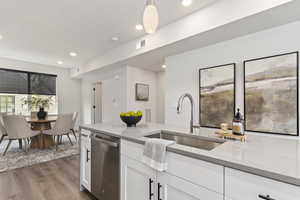 Kitchen featuring light stone counters, white cabinetry, stainless steel dishwasher, hanging light fixtures, and dark wood-style flooring. Model Home