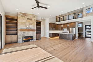 Unfurnished living room with a large fireplace, built in features, light wood finished floors, ceiling fan, and a high ceiling