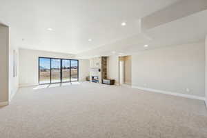 Unfurnished living room featuring light colored carpet, recessed lighting, and a stone fireplace