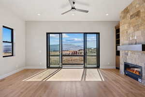Unfurnished living room with a mountain view, light wood-style flooring, a stone fireplace, a ceiling fan, and recessed lighting