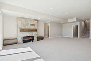 Unfurnished living room with a large fireplace, stairway, light colored carpet, and recessed lighting