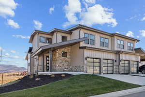 View of front facade featuring stone siding, covered porch, concrete driveway, and a garage