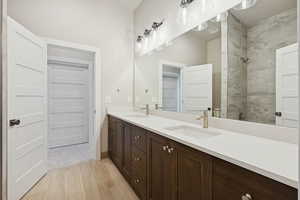 Bathroom with double vanity, a tile shower, and light wood-style floors