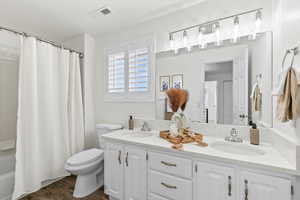 Full bath featuring shower / bath combo, double vanity, updated lighting and dark wood-style floors