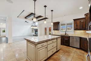 Kitchen with beam ceiling, open floor plan, dark brown cabinets, a stone fireplace, and decorative backsplash