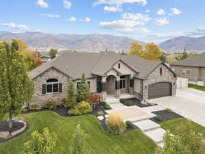 French country inspired facade featuring stone siding, concrete driveway, a mountain view, a front yard, and stucco siding