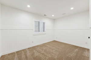 Carpeted empty room with a wainscoted wall and recessed lighting