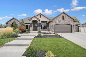 French country style house featuring driveway, a front yard, an attached garage, and stone siding