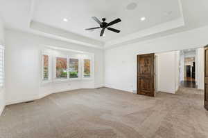 Unfurnished bedroom with a raised ceiling, light carpet, a ceiling fan, and recessed lighting