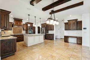 Kitchen with dark brown cabinets, beamed ceiling, decorative backsplash, decorative light fixtures, and light stone countertops