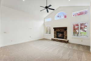 Unfurnished living room featuring high vaulted ceiling, light carpet, a ceiling fan, and a stone fireplace