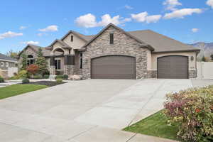 French country style house with a garage, stucco siding, driveway, stone siding, and a mountain view