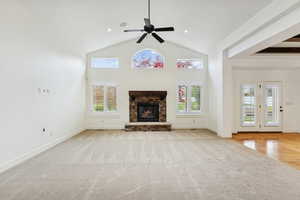 Unfurnished living room with light carpet, a ceiling fan, a stone fireplace, and high vaulted ceiling