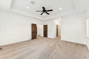 Unfurnished bedroom featuring a raised ceiling, light carpet, a ceiling fan, recessed lighting, and ornamental molding