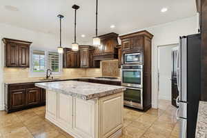 Kitchen with dark brown cabinets, hanging light fixtures, light stone counters, appliances with stainless steel finishes, and recessed lighting