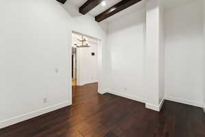 Empty room with beam ceiling, a chandelier, and dark wood-style flooring