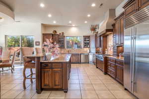 Kitchen featuring glass insert cabinets, appliances with stainless steel finishes, light stone counters, a breakfast bar area, and recessed lighting