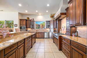 Kitchen with glass insert cabinets, backsplash, light stone countertops, recessed lighting, and light tile patterned floors