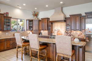Kitchen featuring backsplash, light stone countertops, an island with sink, and recessed lighting