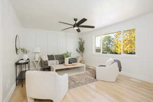 Living room featuring light wood-style flooring, a decorative wall, and ceiling fan