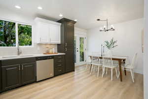 Kitchen featuring white cabinets, stainless steel dishwasher, backsplash, light wood-style flooring, and hanging light fixtures