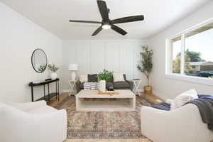 Living room featuring wood finished floors, ceiling fan, and a decorative wall