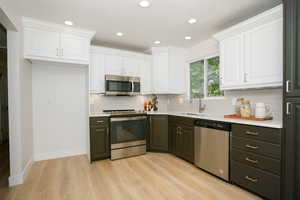 Kitchen with white cabinets, appliances with stainless steel finishes, recessed lighting, tasteful backsplash, and light wood-style flooring