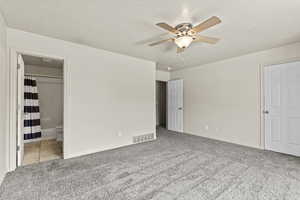 Unfurnished bedroom featuring a textured ceiling, light colored carpet, connected bathroom, and ceiling fan