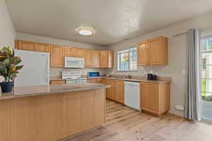Kitchen featuring white appliances, light wood-style flooring, a peninsula, light brown cabinets, and a textured ceiling