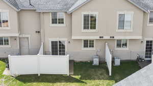 Back of house with a shingled roof, stucco siding, and a lawn