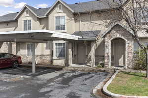 View of front facade featuring stucco siding, stone siding, roof with shingles, and covered parking