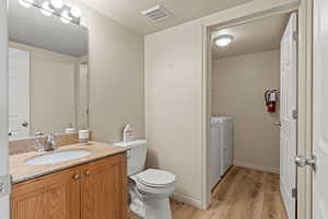 Half bathroom with light wood-style floors, a textured ceiling, vanity, and independent washer and dryer