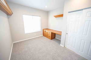 Unfurnished bedroom with light carpet, a closet, and built in desk