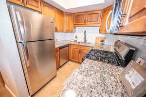 Kitchen with stainless steel appliances, light stone counters, brown cabinetry, tasteful backsplash, and light tile patterned flooring