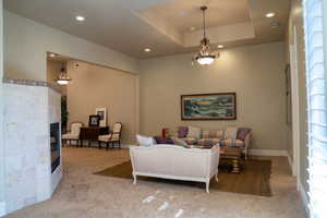 Living room with a raised ceiling, light carpet, a glass covered fireplace, and recessed lighting