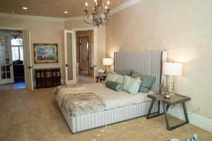 Carpeted bedroom with a textured wall, crown molding, and a chandelier