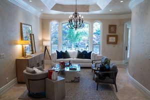 Living room featuring ornamental molding, a textured wall, a chandelier, and a tray ceiling