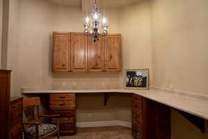 Unfurnished office with built in desk, a chandelier, and dark colored carpet