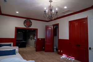 Bedroom featuring a chandelier, ornamental molding, light colored carpet, wainscoting, and wood walls