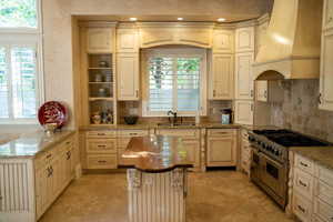 Kitchen with double oven range, open shelves, custom exhaust hood, light stone countertops, and decorative backsplash