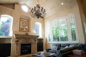 Living room with a fireplace, a chandelier, high vaulted ceiling, and a textured wall