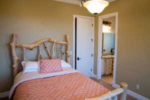 Bedroom with ensuite bath, light carpet, and ornamental molding