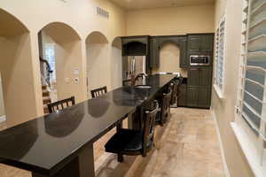 Kitchen featuring a kitchen breakfast bar, stone tile floors, stainless steel appliances, dark stone counters, and an island with sink