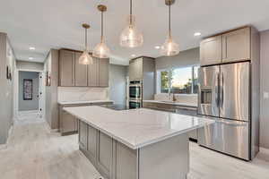 Kitchen with stainless steel appliances, decorative light fixtures, light stone counters, light wood finished floors, and a center island