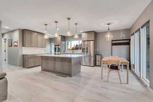Kitchen with gray cabinetry, a center island, stainless steel fridge with ice dispenser, pendant lighting, and light wood-style floors