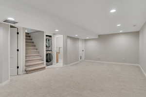 Finished basement with recessed lighting, stacked washer / drying machine, light carpet, and stairway